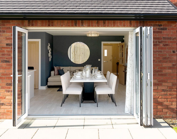 Bi-fold doors opening onto a paved patio and large turfed gardens